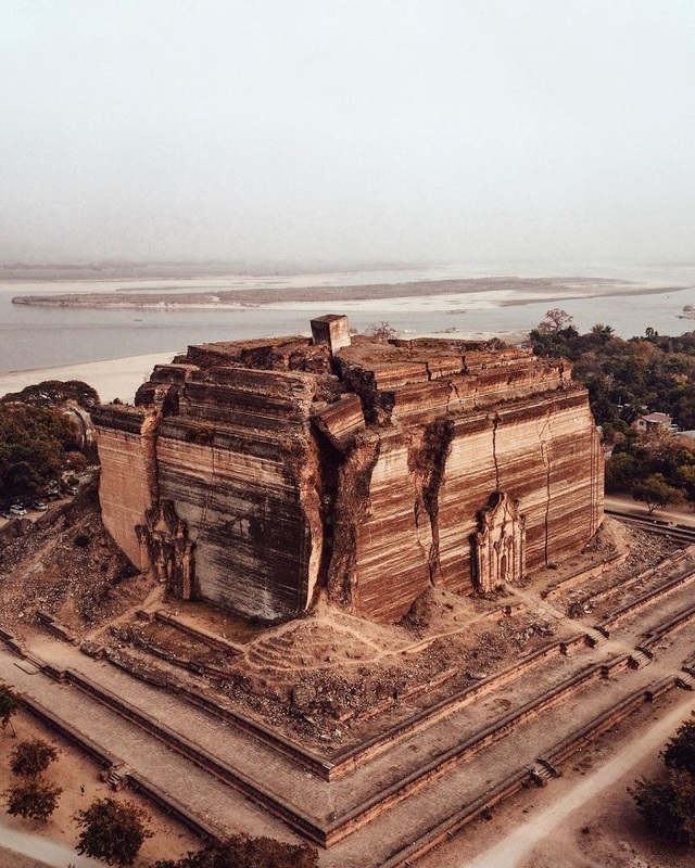 A stunning aerial view of the unfinished Mingun Pahtodawgyi Stupa, standing tall by the serene Irrawaddy River, despite the scars of time.