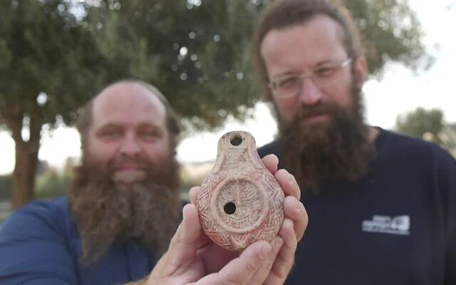 In a photograph released on December 26, 2024, Michael Chernin and Benjamin Storchan present a 1,700-year-old oil lamp featuring a Temple menorah design, unearthed in Jerusalem. (Image credit: Emil Aladjem/Israel Antiquities Authority)