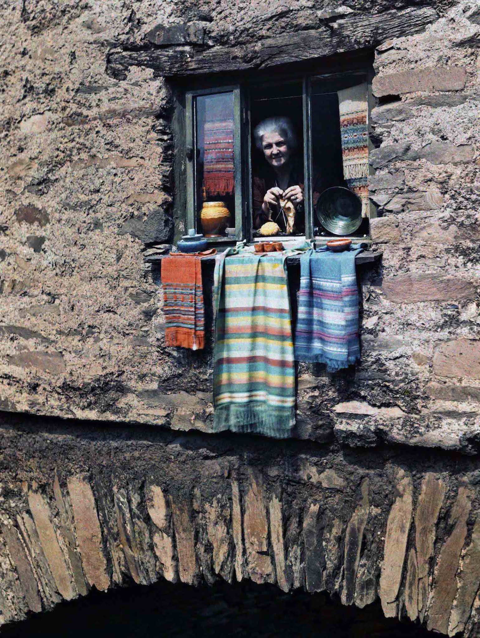 A Cozy View in the Lake District – A woman peeks out from her charming bridge house window in Ambleside, Cumbria.