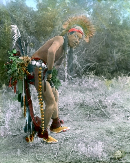 A Crow dancer, dressed in traditional regalia, captured in a stunning portrait in the early 1900s by Richard Throssel.