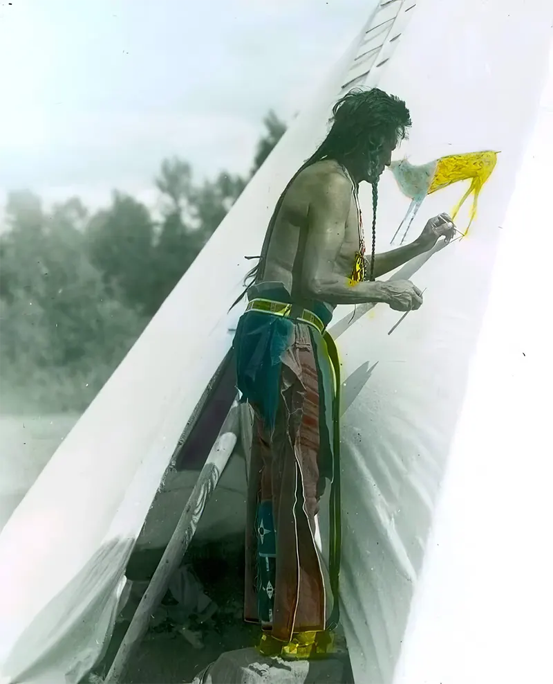 A Crow man carefully painting his tipi, possibly marking it with “the sign of his medicine,” as described by the photographer. Montana, early 1900s.