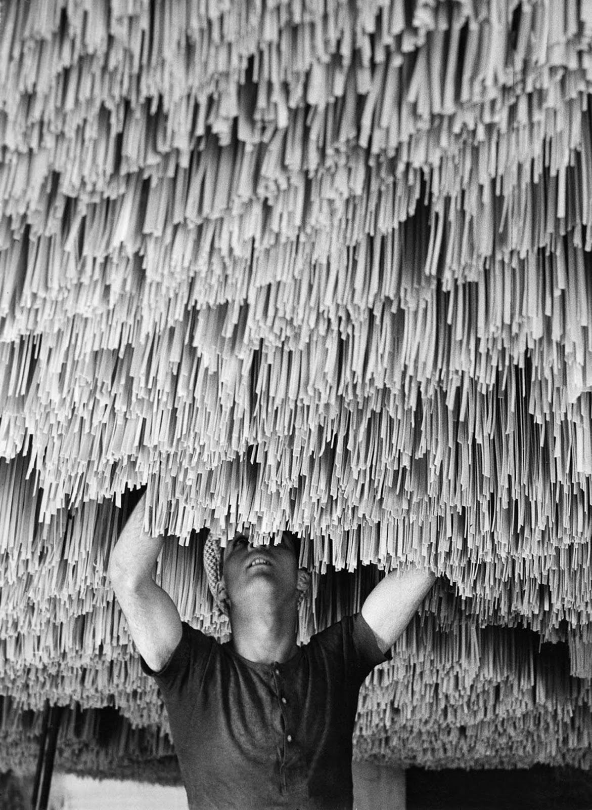 A factory worker carefully hangs pasta to dry in Italy, ensuring the perfect texture. 1932.