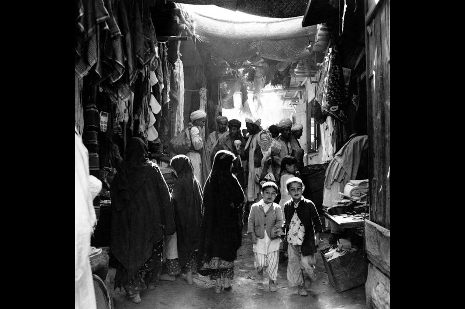 A glimpse into Kabul’s markets in May 1964, where barefoot shoppers browse through stalls of fresh produce.