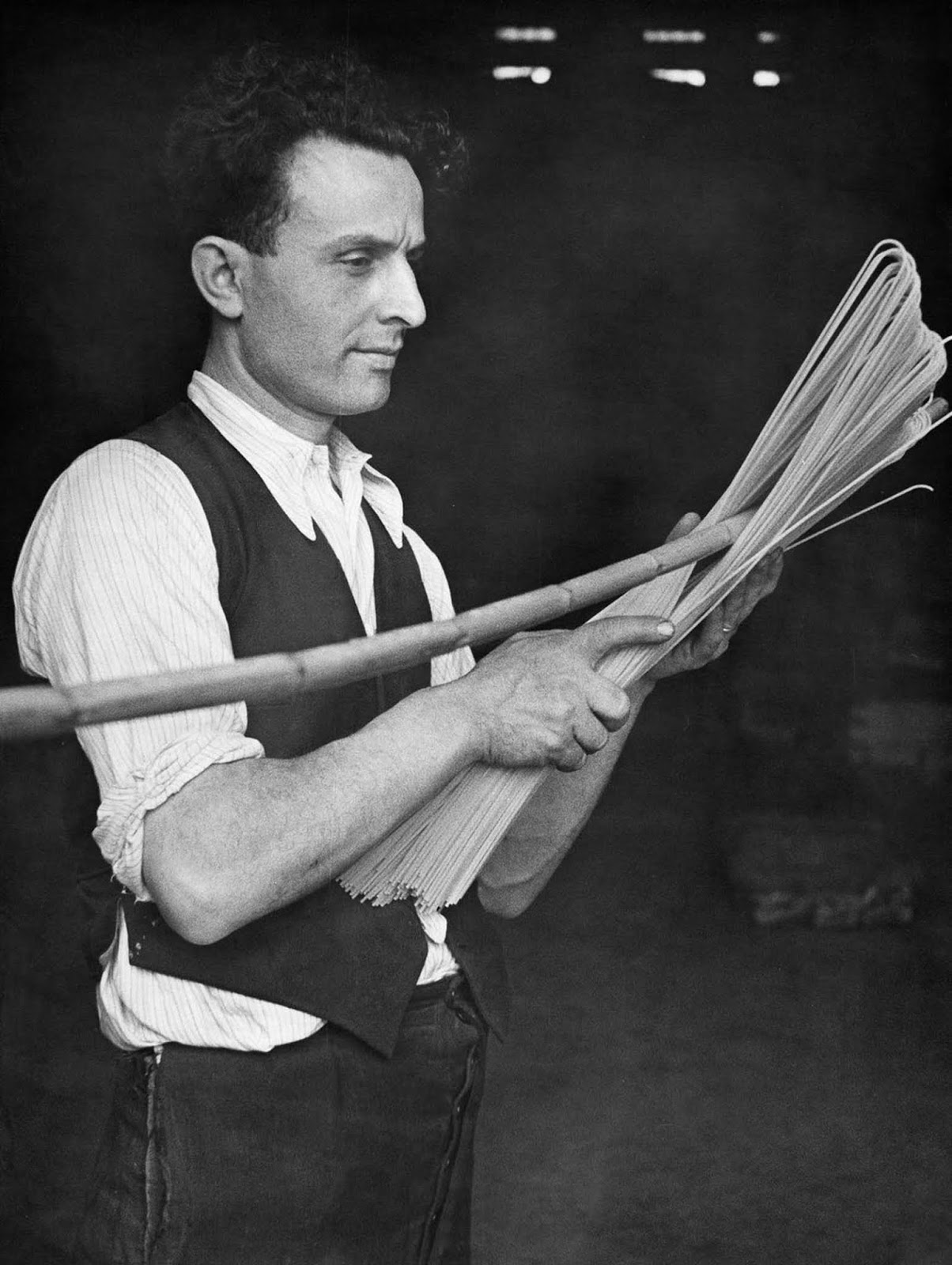 A pasta factory worker skillfully bends spaghetti with a stick, shaping it to perfection. 1932.