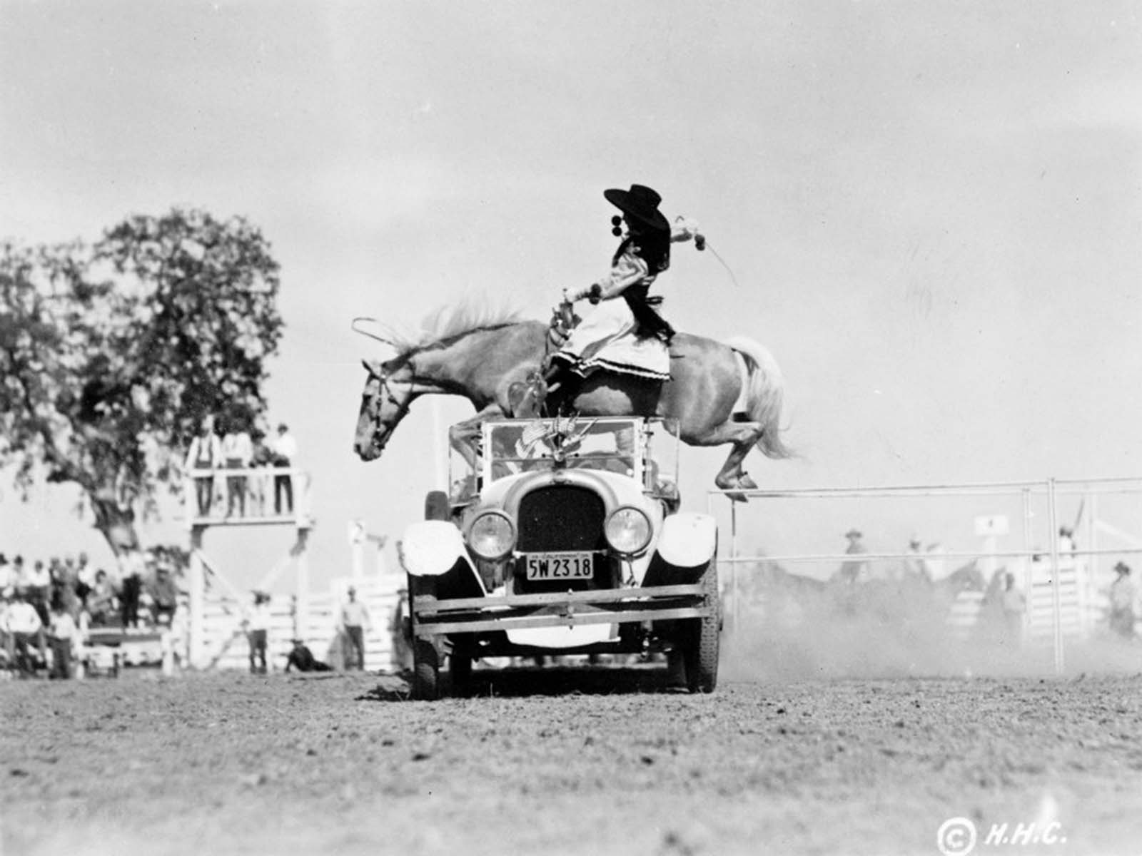 A skilled cowgirl and her horse leap over a convertible at a California rodeo, 1934.