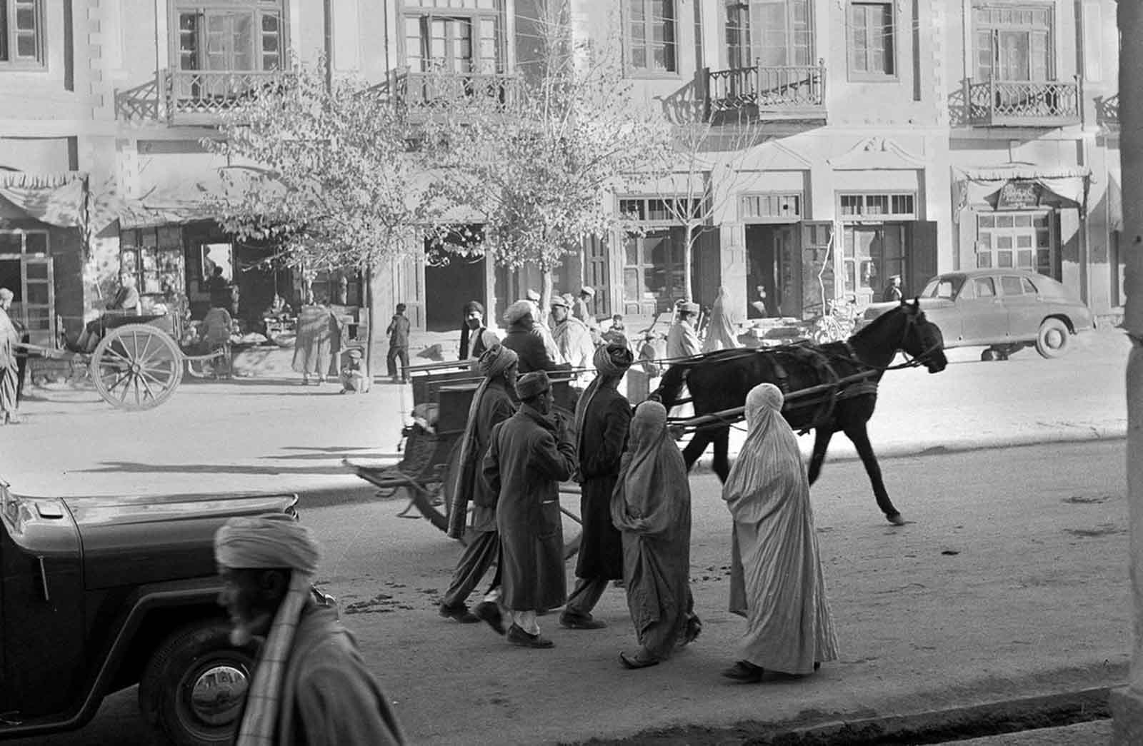 A snapshot of Kabul’s evolving transportation scene, where burqa-clad women walk alongside cars and horse carts, 1951.