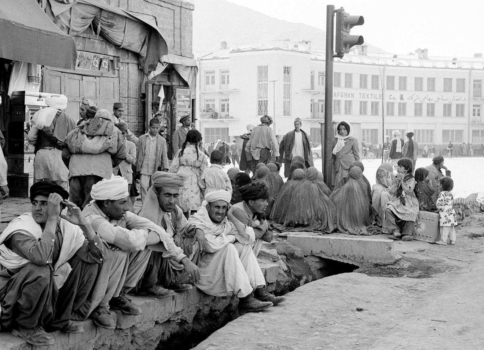 A striking contrast—a modern traffic light stands near burqa-clad women seated on a Kabul street corner, May 25, 1964.