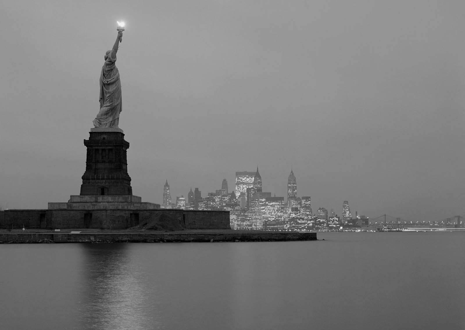 A stunning 1961 evening photograph captures the Statue of Liberty with the illuminated Manhattan skyline in the background.