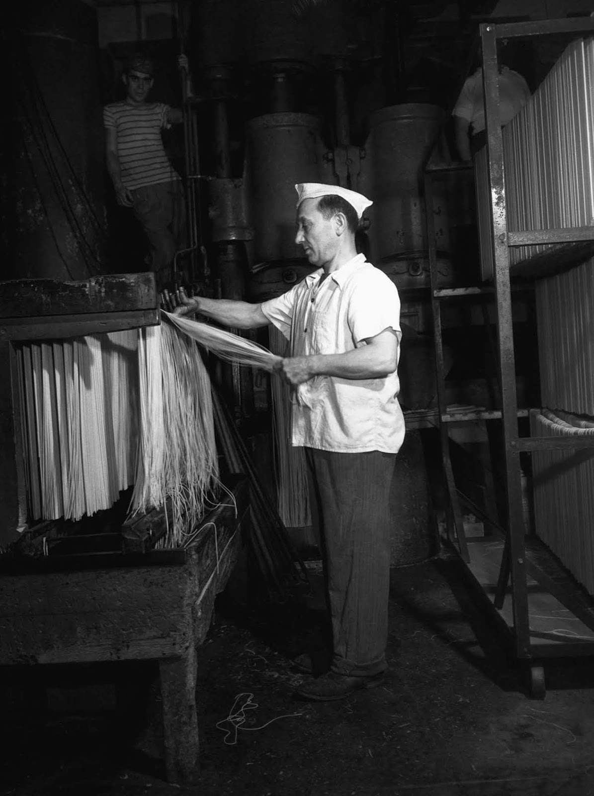 A worker at the Atlantic Macaroni Company hangs fresh spaghetti to dry at a New York factory. 1943.