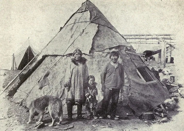 An Inuit family stands proudly in front of their summer home, photographed in 1915.