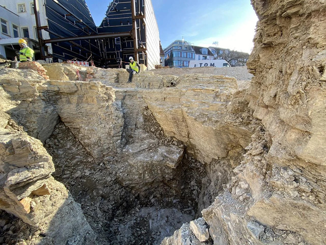 Archaeologists at work in the exposed quarry site, revealing the extent of the ancient stone excavation beneath the modern buildings.