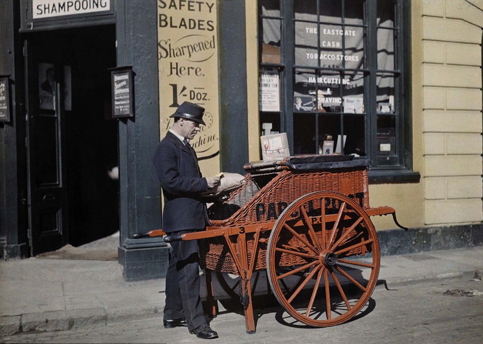 Delivering with Care – A postman pushes his parcel post barrow while making deliveries outside a barber shop in Oxford in 1928.