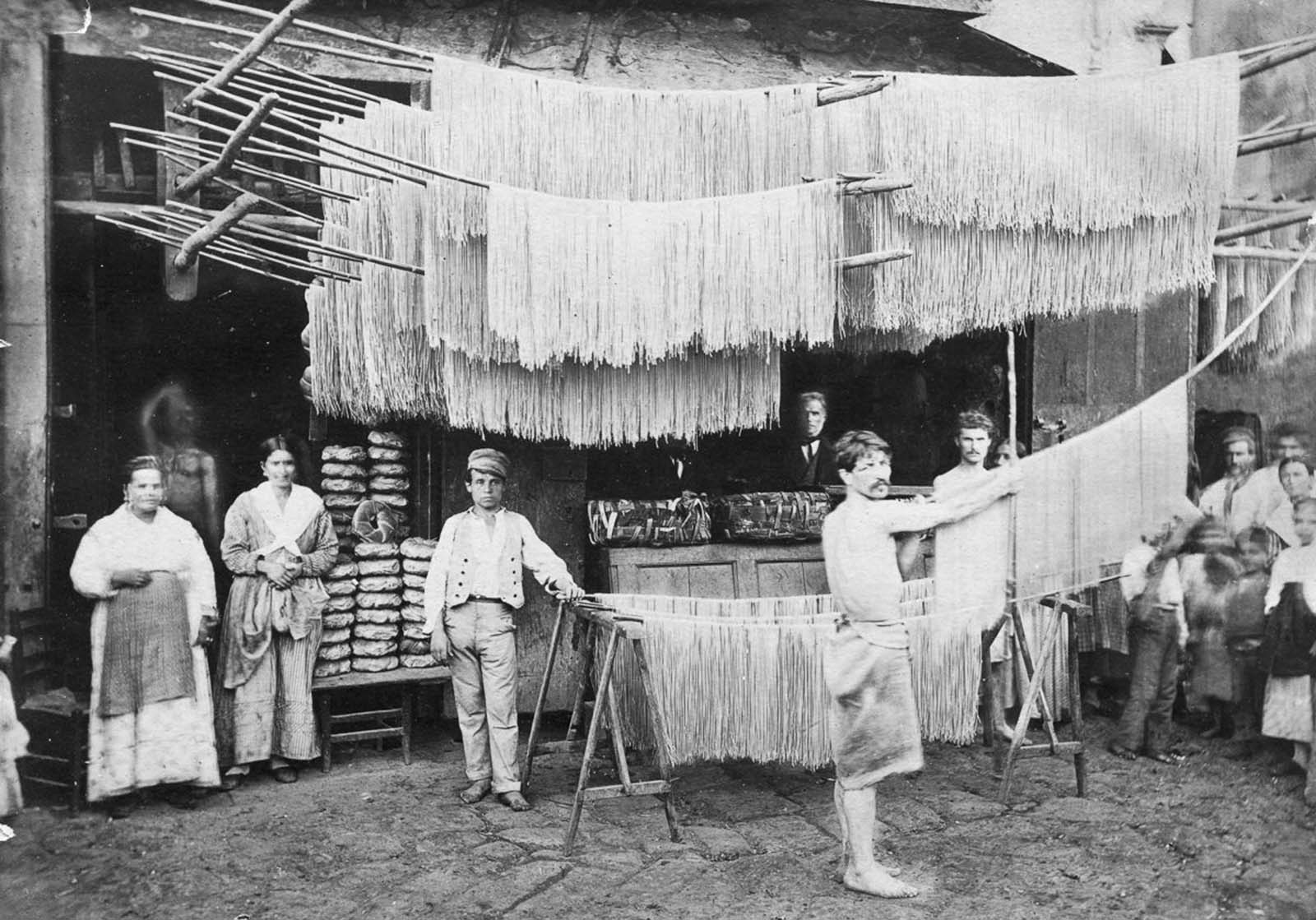 Freshly made pasta hangs to dry in a bustling Italian market, a common sight in the past. Date unknown.