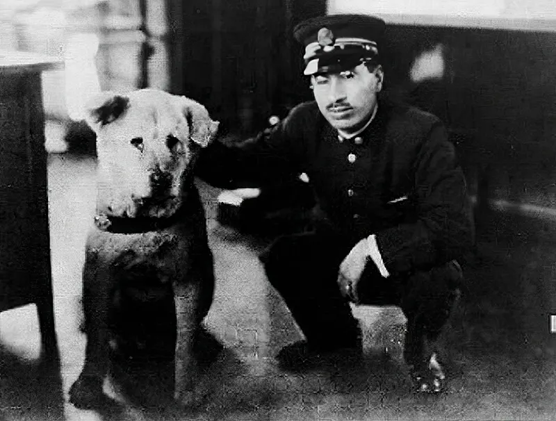 Hachikō sits beside a train conductor at Shibuya Station, a quiet companion to those passing by.