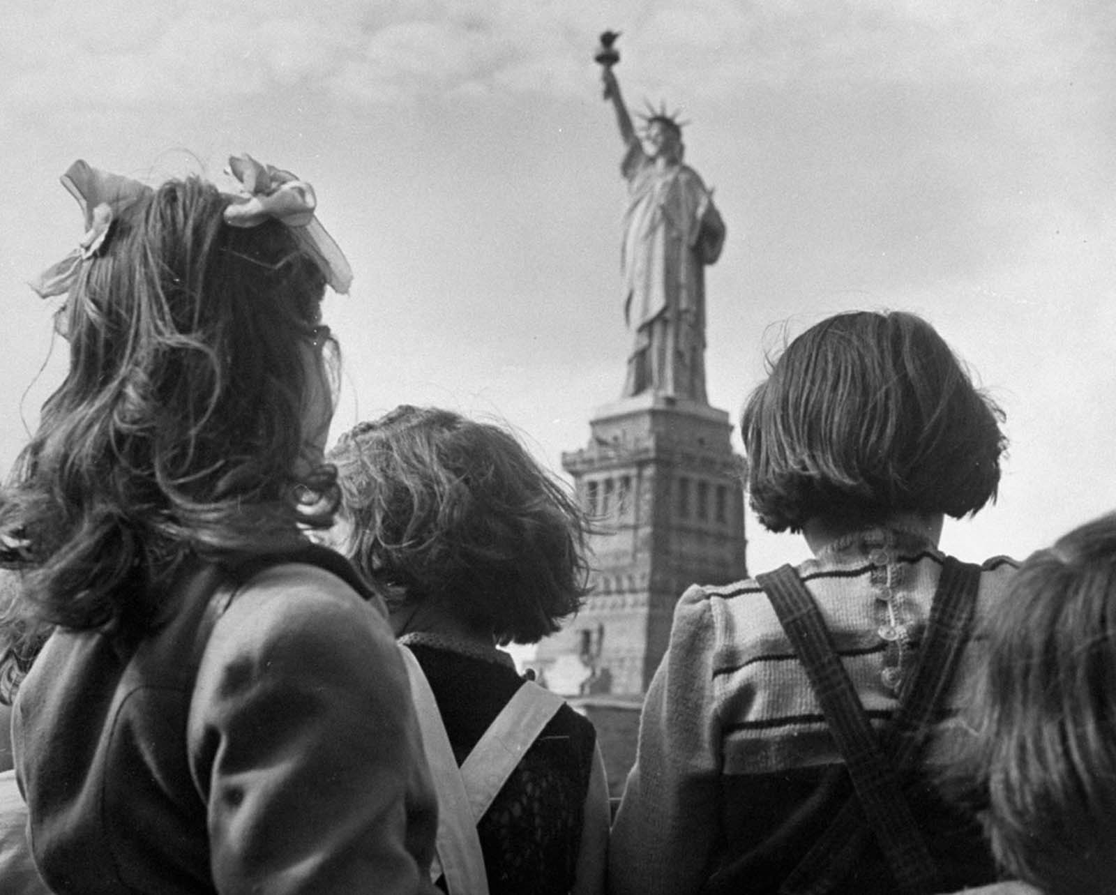 In a poignant moment from 1946, refugee children gaze at the Statue of Liberty from the railing of their boat, seeing their new home for the first time.