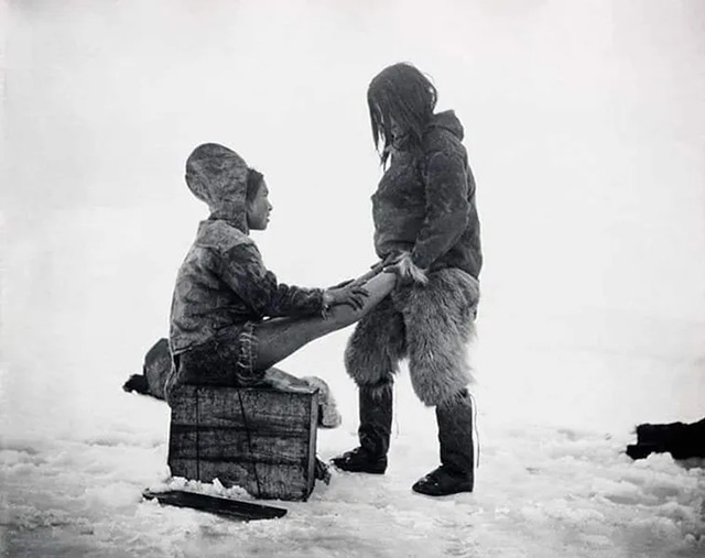 In the 1890s, an Inuit man lovingly warms his wife’s feet in Greenland, captured by Robert E. Peary.