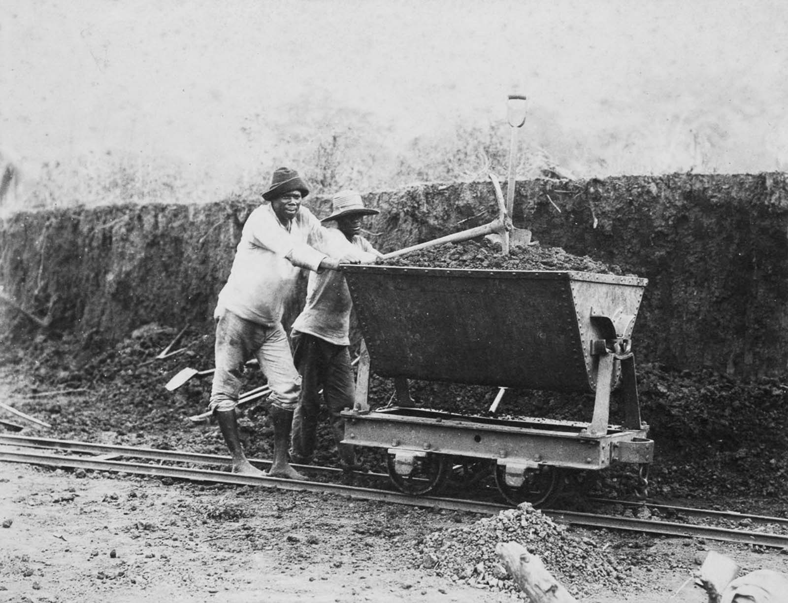 Jamaican workers push a loaded wagon along a narrow-gauge railroad, transporting excavated earth in 1885.