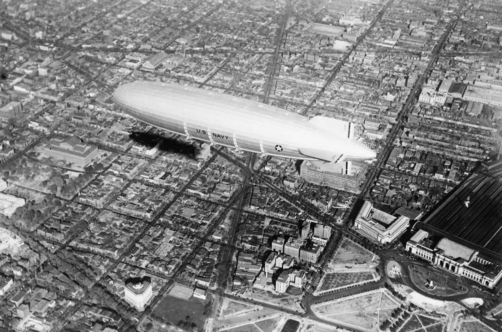 The USS Akron hovers over Washington, D.C., in 1931, casting a long shadow over New Jersey Avenue and Massachusetts Avenue below.