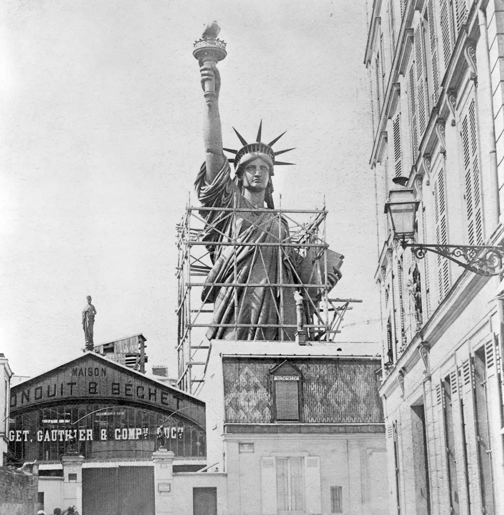 The fully assembled Statue of Liberty dominates the Paris skyline, towering over surrounding buildings before its disassembly and shipment to America.