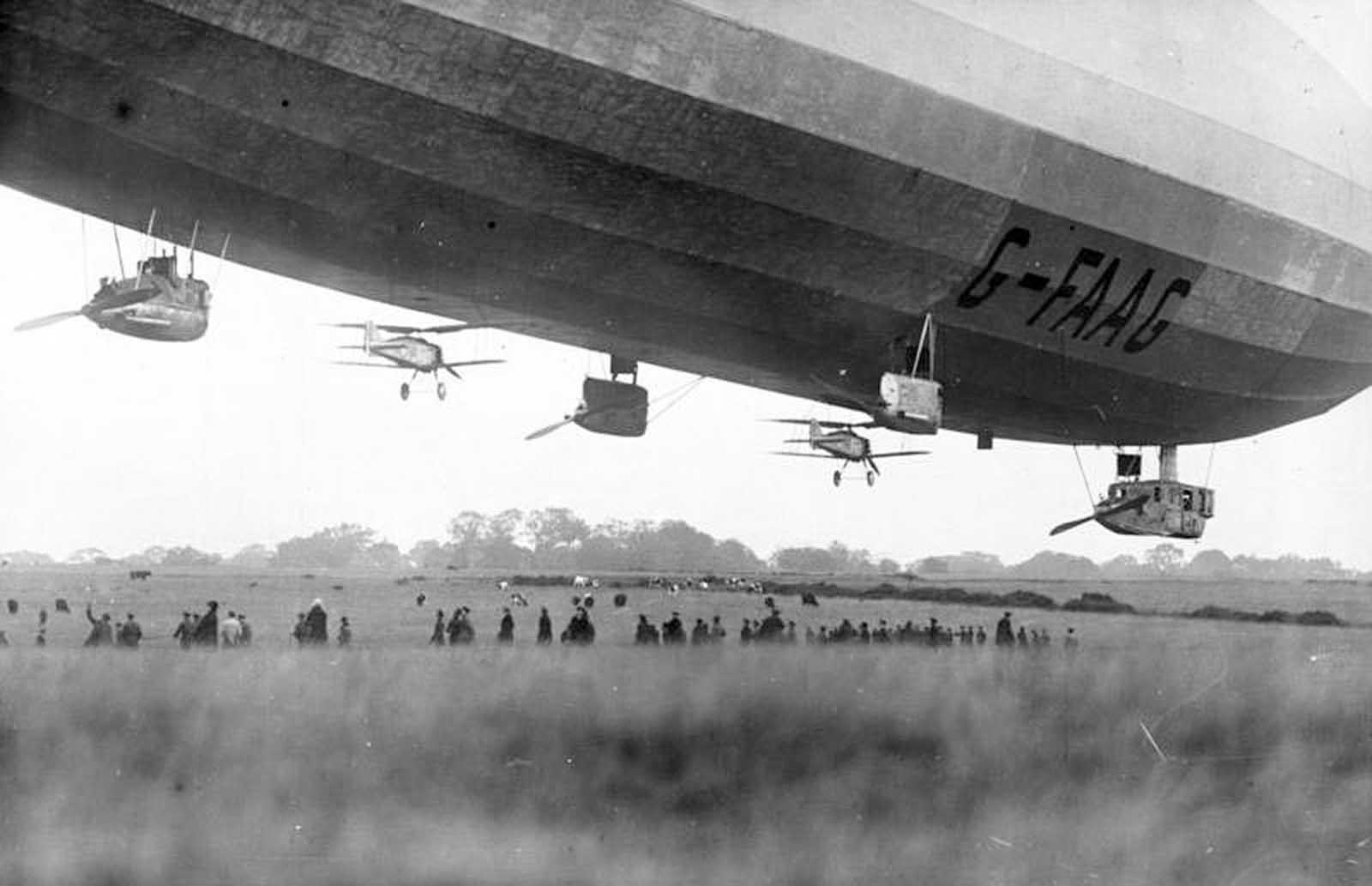 Two Gloster Grebe fighter planes are tethered beneath the British Royal Navy airship R33 in October 1926, testing air-launch capabilities.