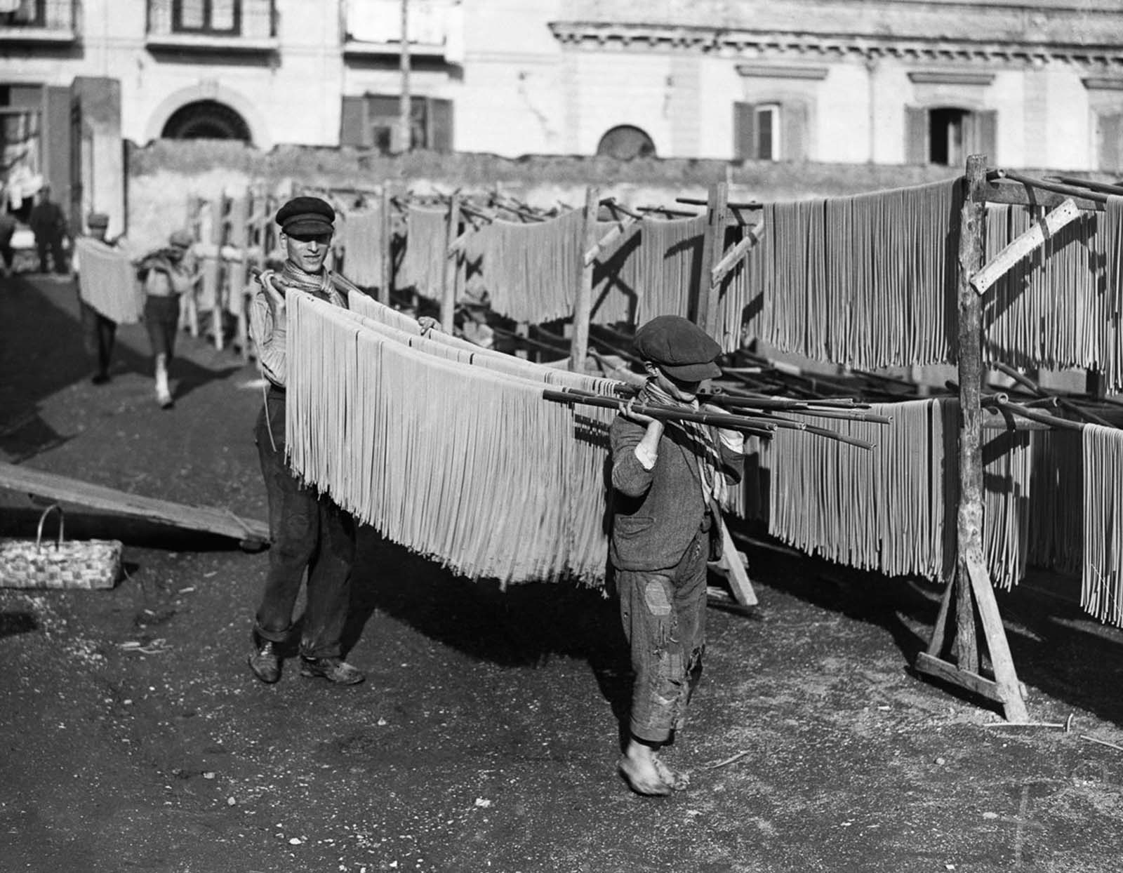 Young boys carry long strands of pasta to the factory yard for drying, ensuring it cures perfectly. Date unknown.