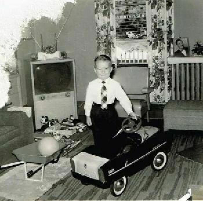 A little boy proudly standing by his new pedal car, 1958.