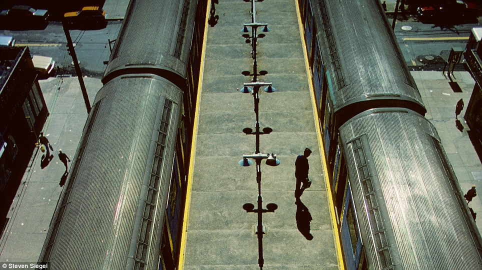 From above the subway station, a figure steps into the train, casting long shadows across the platform in this striking composition.